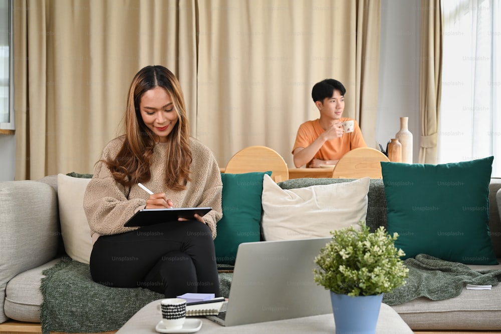 Cheerful asian woman sitting in living room with her husband and using digital tablet.