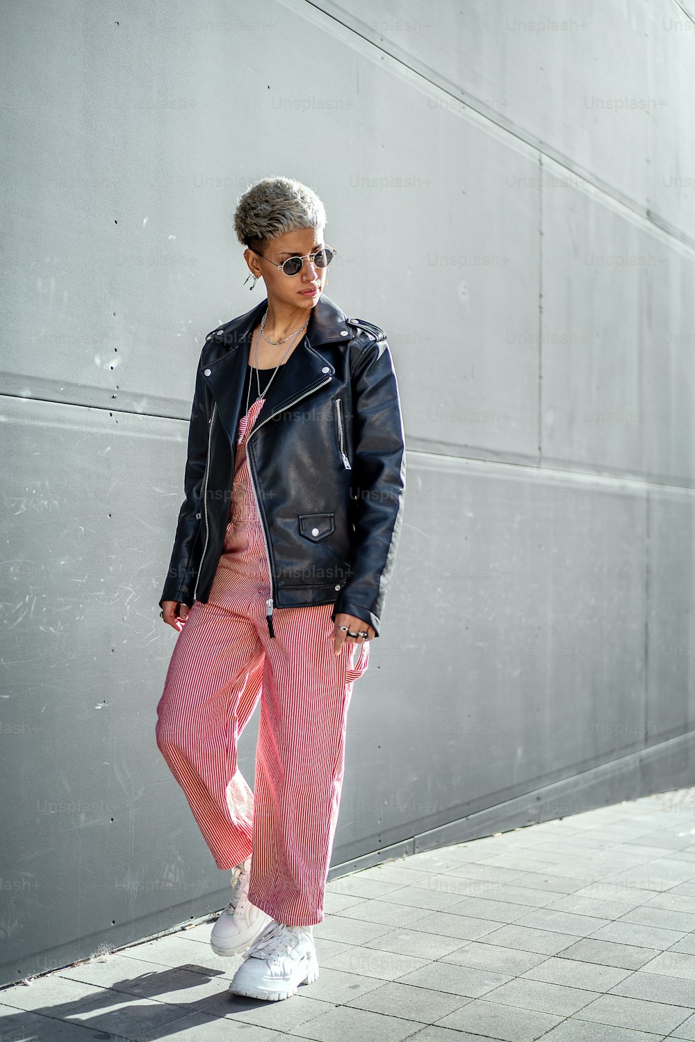 Fashionable modern young woman wearing sunglasses and black jacket, walking on the city street. A lot of copy space.