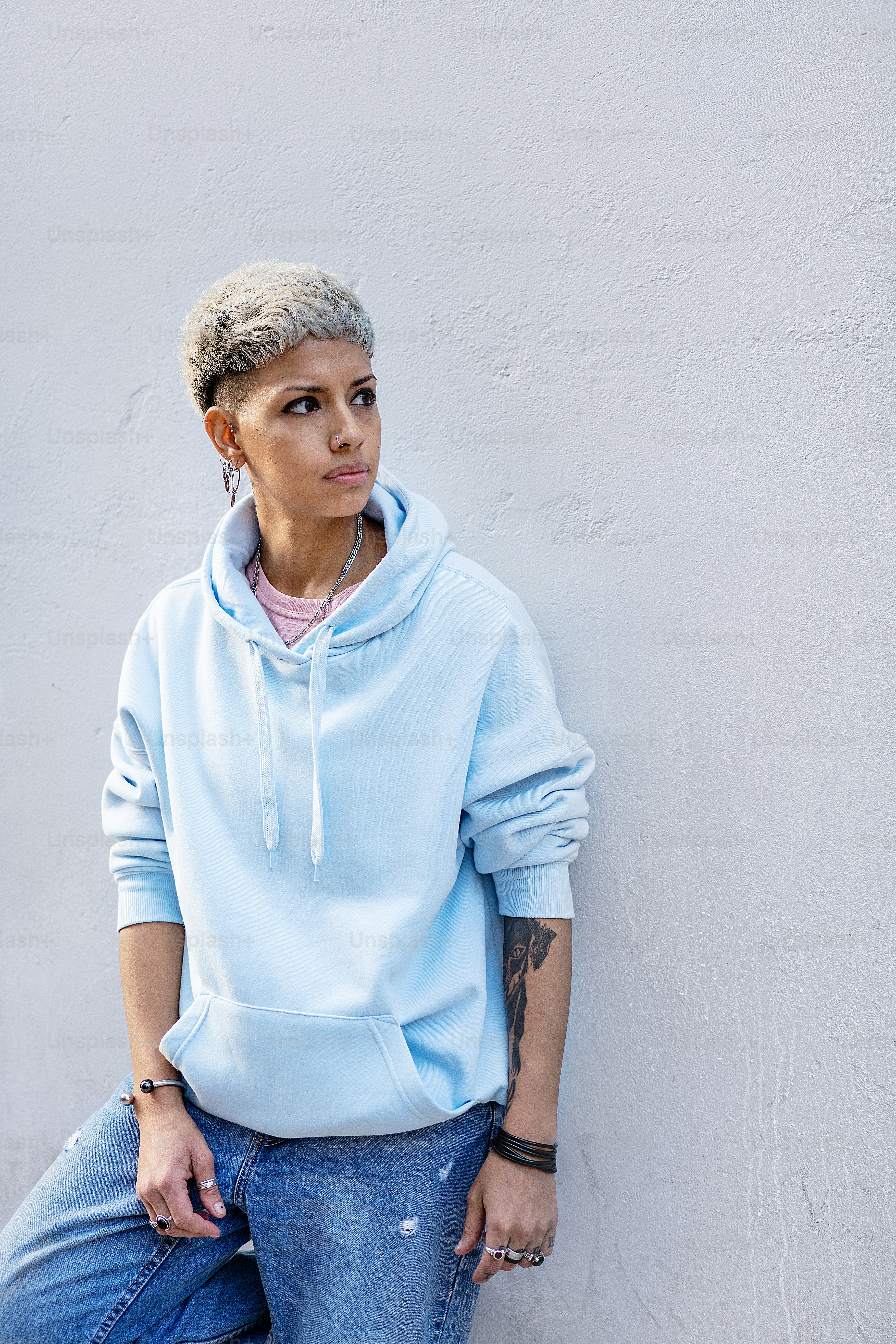 Fashionable young woman wearing blue hoodie and jeans posing on the city wall. Blonde girl in short hairstyle.