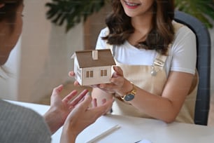Agente inmobiliario recortado que sostiene el modelo de la casa y da una propuesta al cliente.