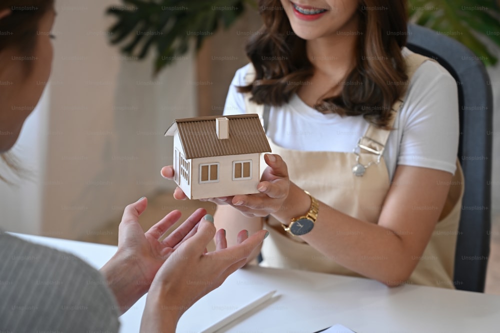 Cropped shot real estate agent holding house model and give proposal to customer.