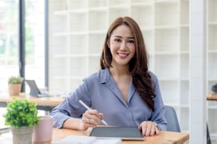 Beautiful young Asian businesswoman sitting looking at camera with laptop in office.