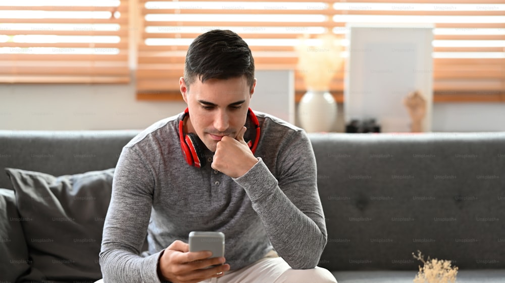 Young man checking social media on smartphone while sitting in living room.
