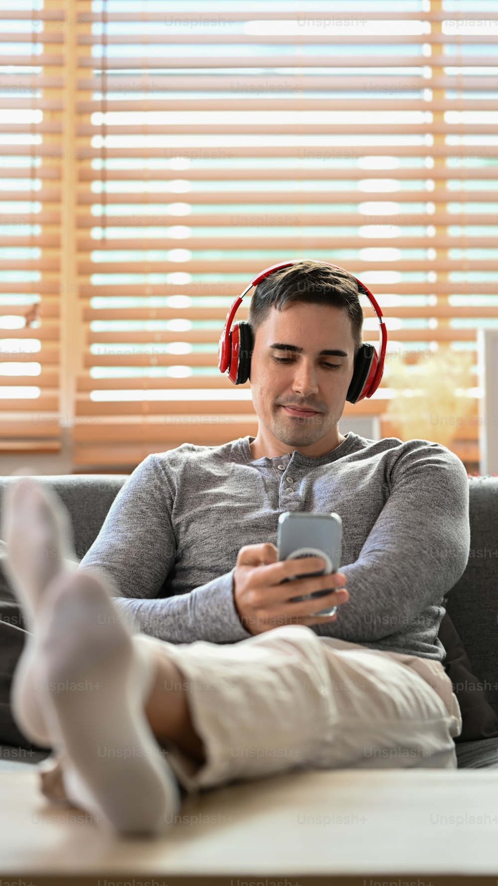 Jeune homme heureux portant des écouteurs et utilisant un téléphone intelligent sur le canapé.
