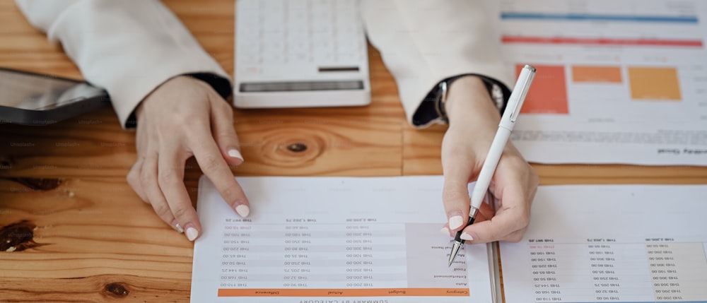 Cropped image of businesswoman analyzing financial document on wooden table.