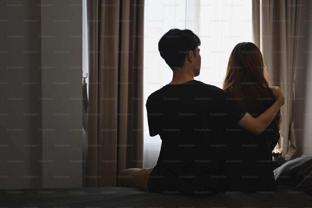 Back view of young man embracing his wife and sitting in bed room. Comforting, encouraging and understanding.