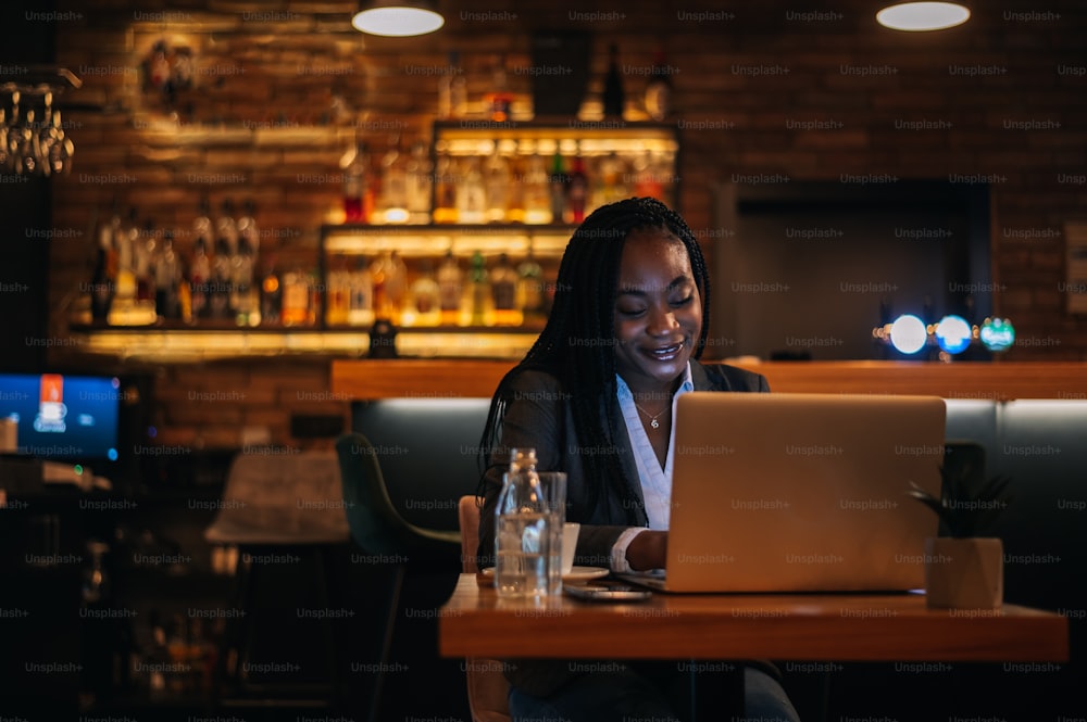 Junge schöne afroamerikanische Geschäftsfrau arbeitet an ihrem Laptop, während sie in einem Café Kaffee trinkt