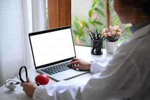 Female doctor in white uniform working with laptop computer at medical office.