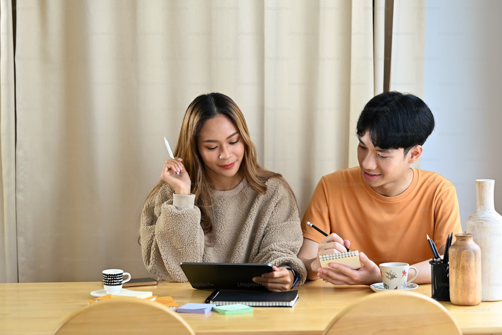 Feliz jovem casal asiático sentado juntos na sala de estar brilhante e navegando internet com tablet digital.