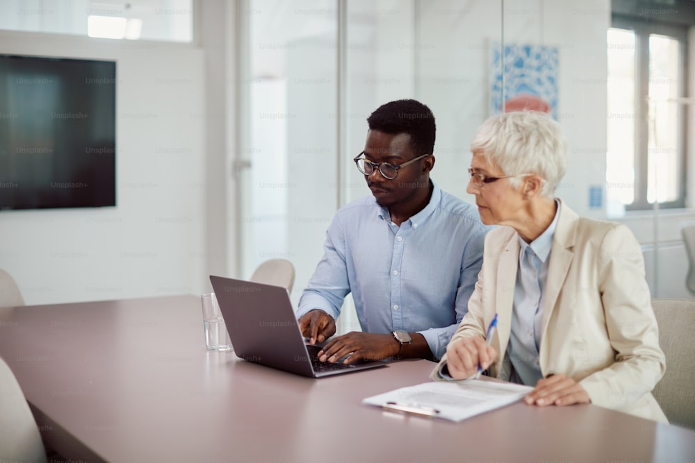 Young African American businessman using laptop while working with senior colleague int he office.