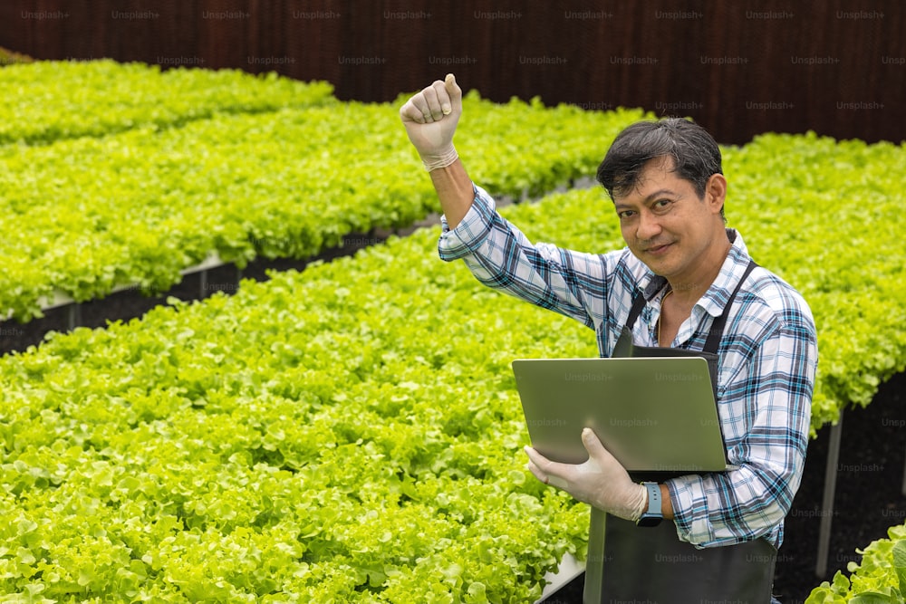 In a greenhouse environment, an agricultural researcher examines plants with a laptop computer while holding the laptop.