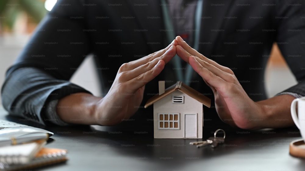 L'agente immobiliare consegna il modello di casa per la protezione e la cura. Concetto di assicurazione sulla proprietà.