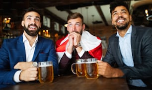 Hombres de negocios, aficionados gritando y viendo fútbol en la televisión y bebiendo cerveza en un pub
