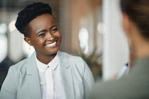 Happy African American corporate manager talking to her female coworker while working in the office.