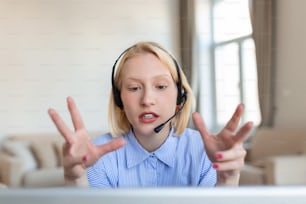 Porträt einer blonden Frau, die Videoanrufe mit dem Laptop macht. Geschäftsfrau mit Headset spricht während des Online-Meetings mit Kollegin. Albino-Frau, die von zu Hause aus über eine Videokonferenz am Computer arbeitet.