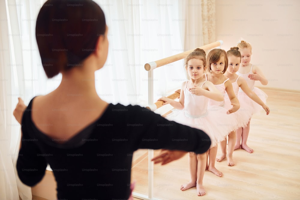 Coach teaches children. Little ballerinas preparing for performance by practicing dance moves.
