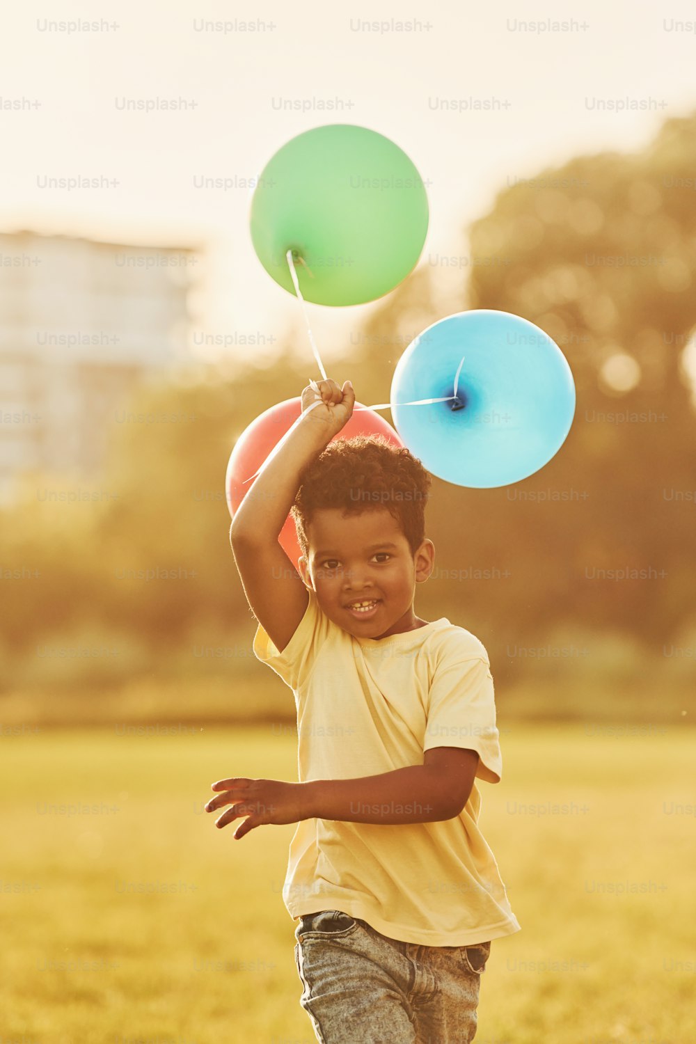 With balloons in hands. African american kid have fun in the field at summer daytime.