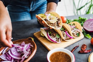 latin woman hands preparing mexican tacos with pork carnitas, avocado, onion, cilantro, and red sauce in Mexico