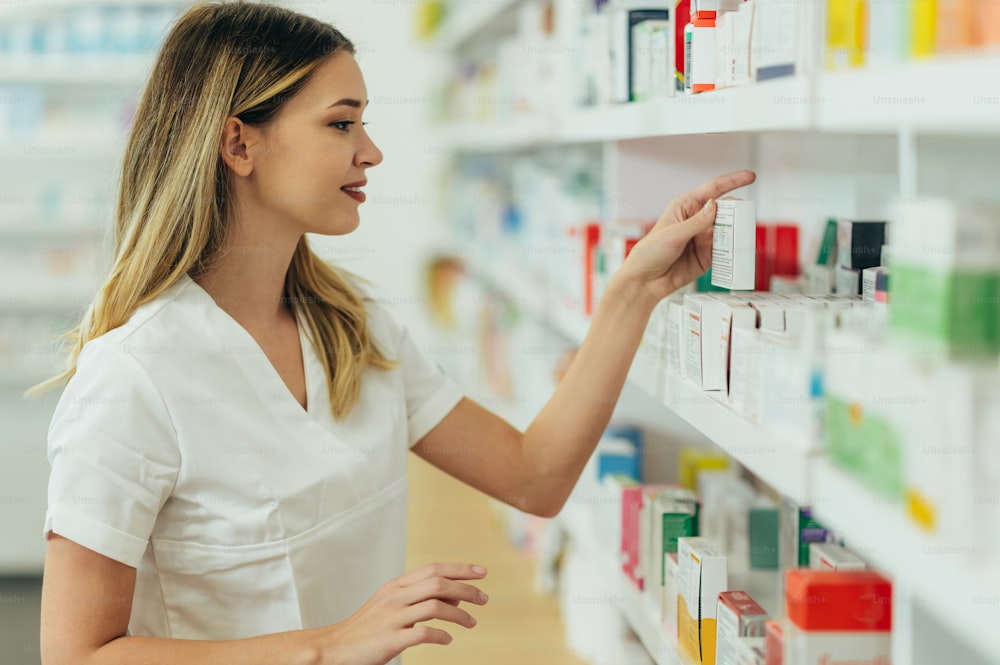 Ritratto di una bella farmacista femminile che lavora in una farmacia e controlla i farmaci su uno scaffale