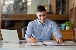 Businessman working on laptop and taking notes in office.