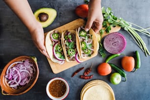 mãos da mulher latina preparando tacos mexicanos com carnitas de porco, abacate, cebola, coentro e molho vermelho no México