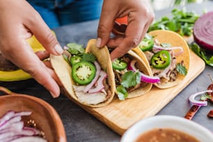 latin woman hands preparing mexican tacos with pork carnitas, avocado, onion, cilantro, and red sauce in Mexico