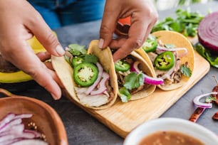 mani di donna latina che preparano tacos messicani con carnitas di maiale, avocado, cipolla, coriandolo e salsa rossa in Messico