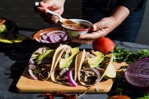 latin woman hands preparing mexican tacos with pork carnitas, avocado, onion, cilantro, and red sauce in Mexico