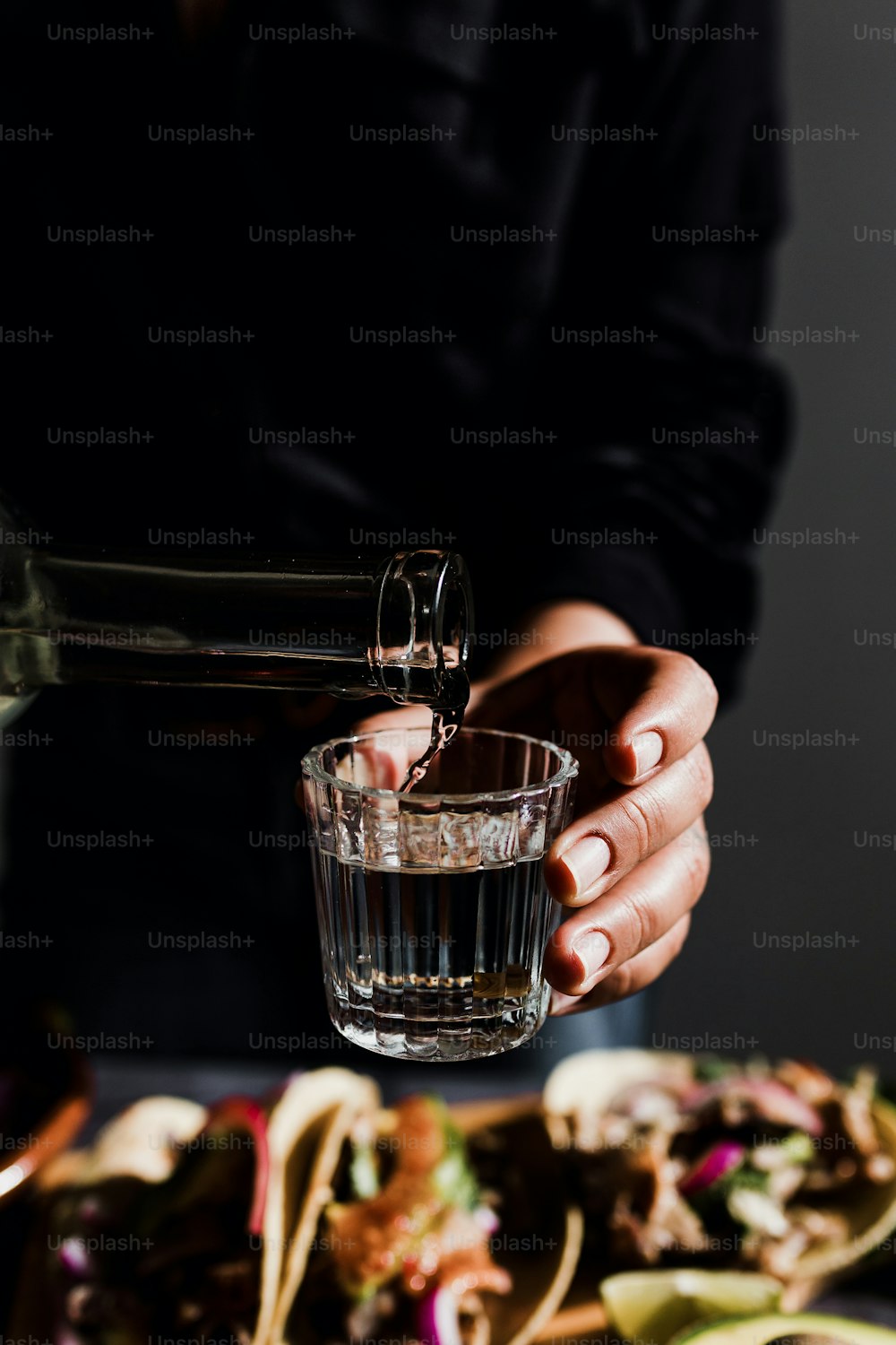 Mani del barman che servono mezcal messicano girato in un bicchiere tradizionale con tacos e cibo sullo sfondo in Messico