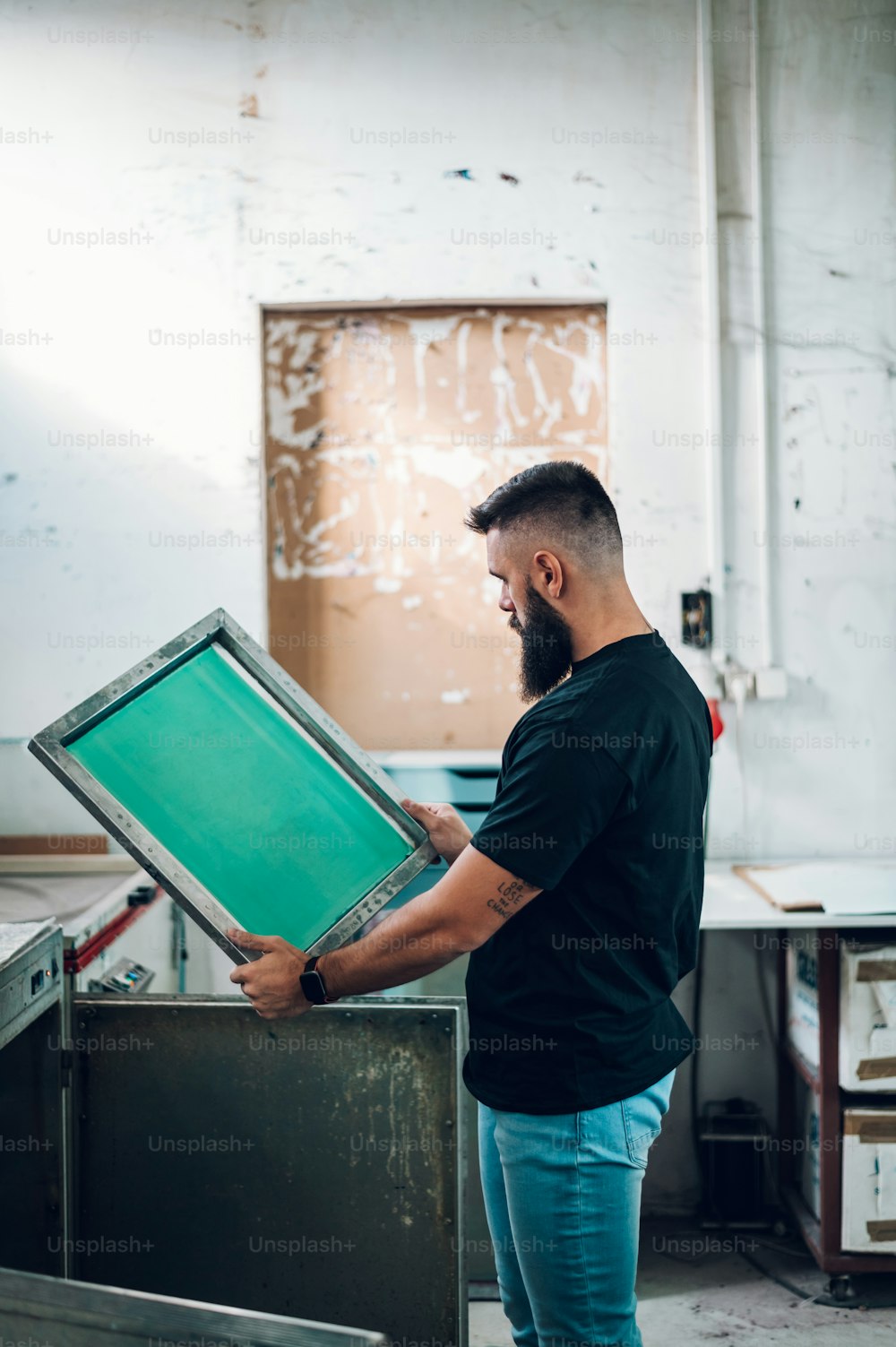 Male worker holds the silkscreen frame and carefully observes the resulting film in a printing workshop