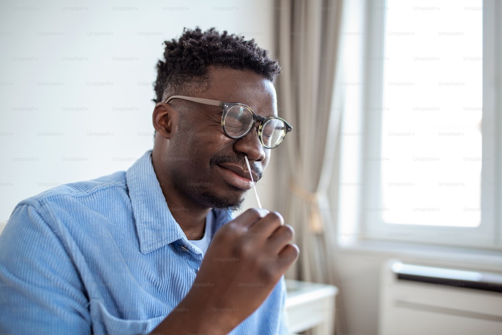 Shot of a African man using cotton swab while doing coronavirus PCR test at home. man using coronavirus rapid diagnostic test. Young man at home using a nasal swab for COVID-19.