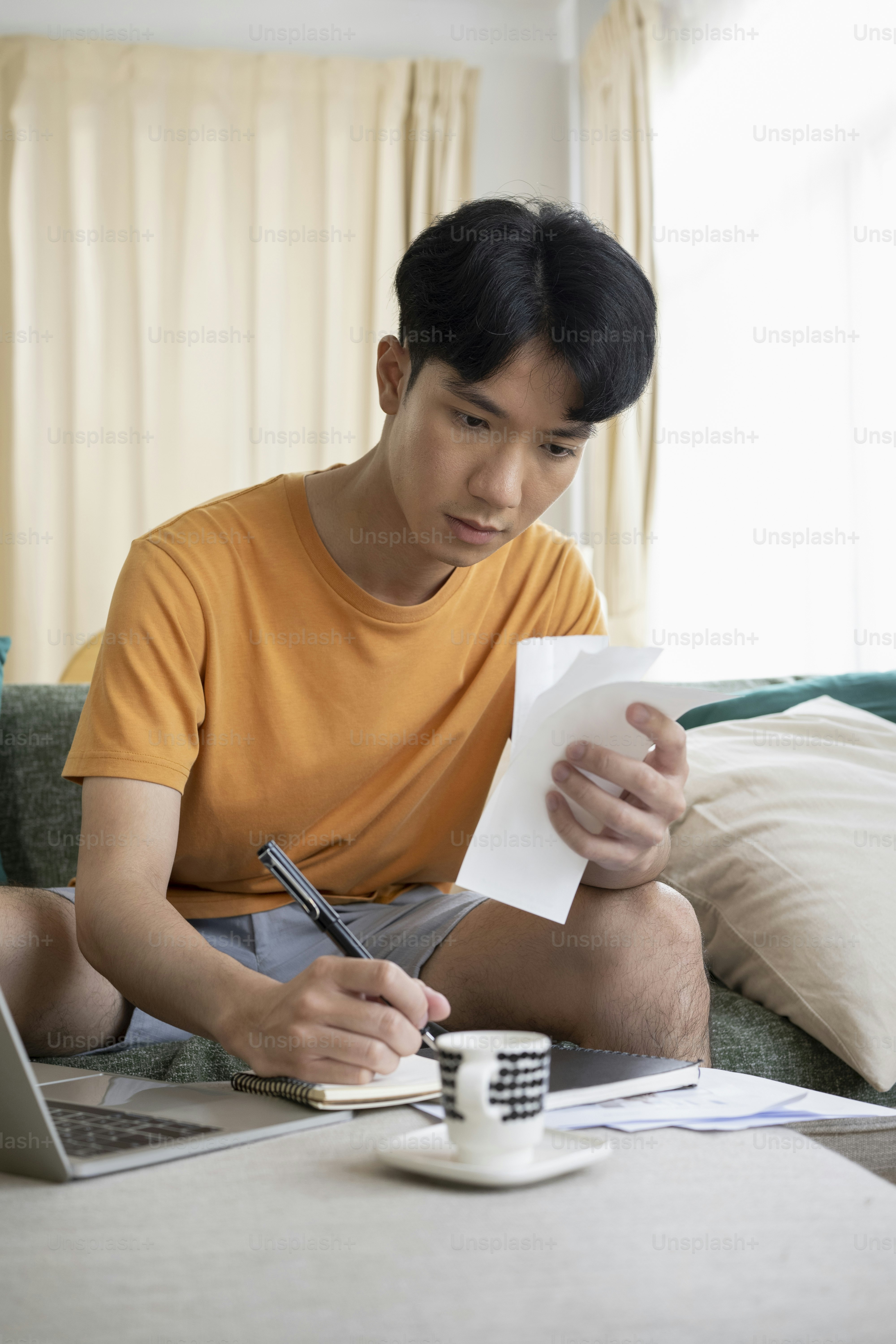 Busy young asian man sitting on couch and calculating household bills.