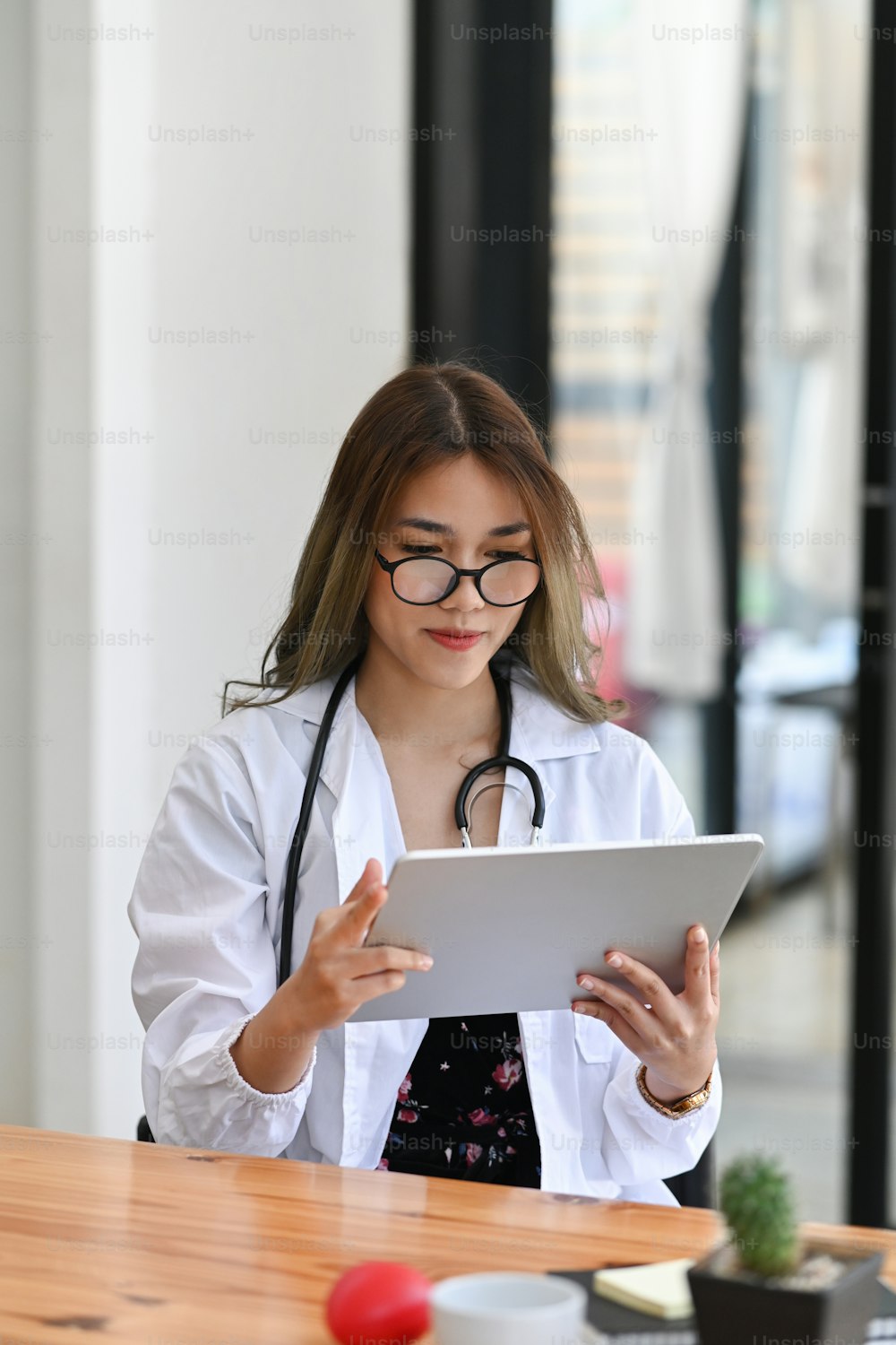 Portrait of attractive female doctor white uniform using digital tablet while sitting in medical office.