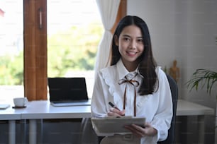Charming young businesswoman holding digital table and looking at camera.