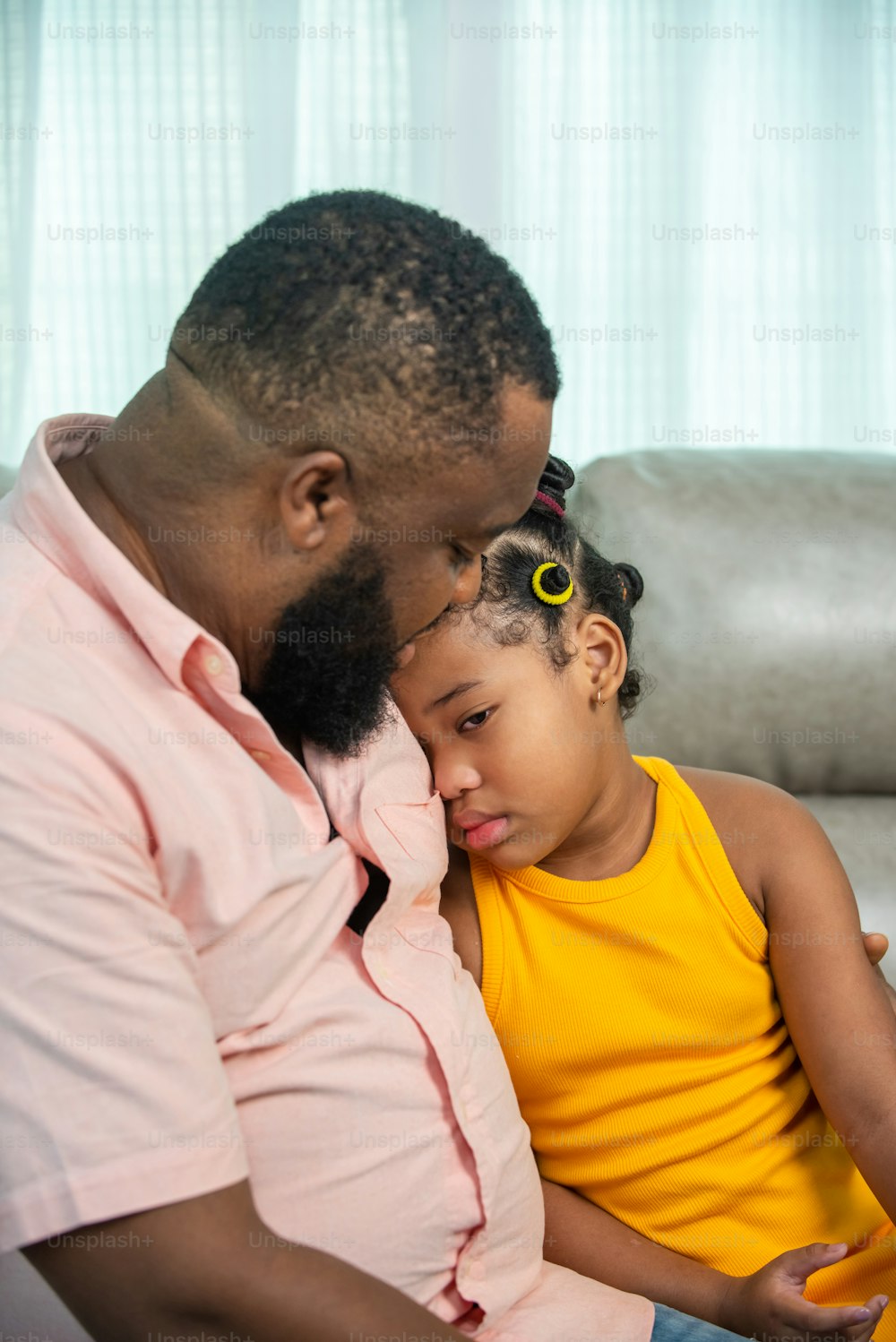 Happy African family spending time together at home. Father sitting on sofa in living room with comforting sad little girl daughter. Family relationship and children mental health social issue concept