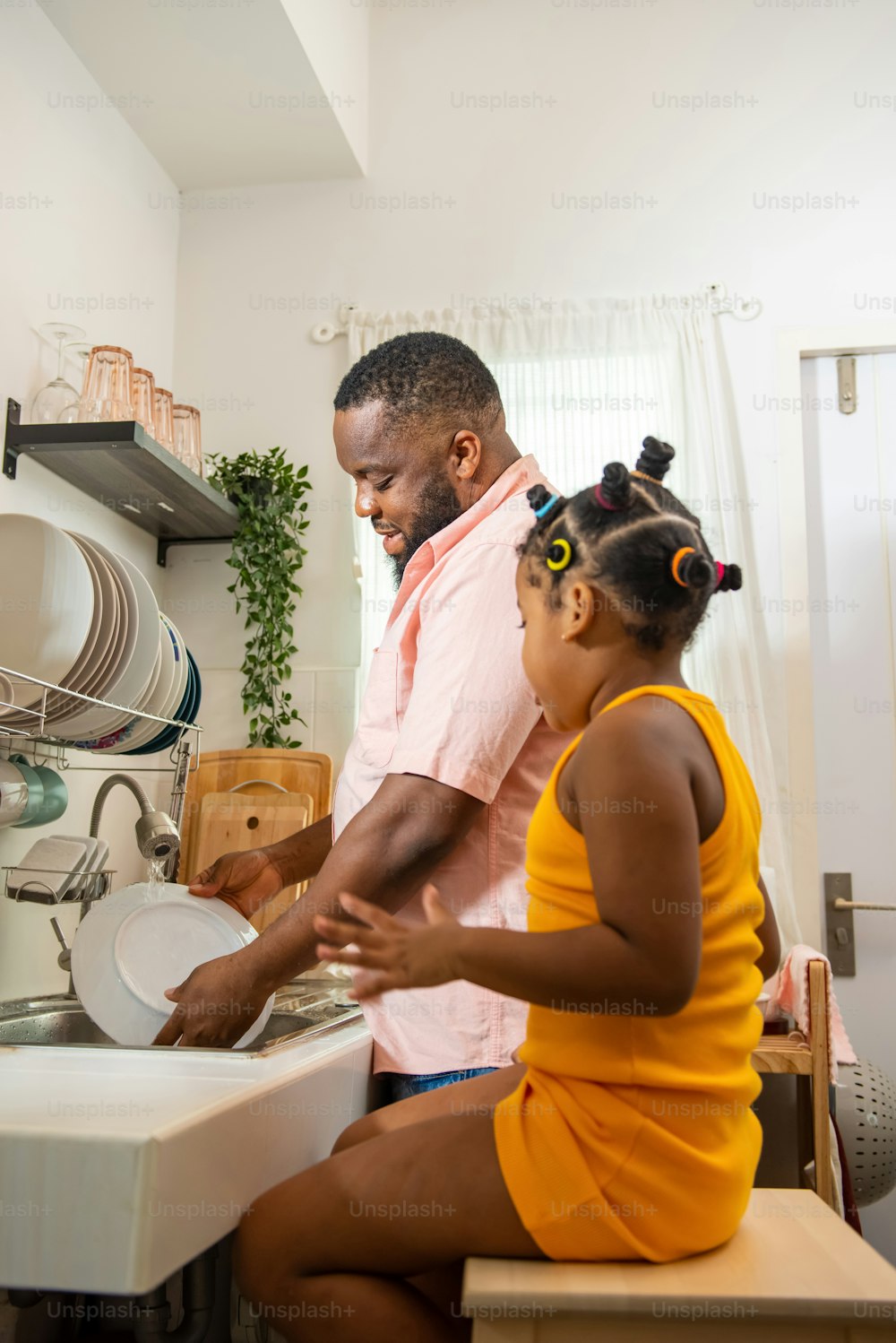 African father teaching little daughter washing dishes in the sink on kitchen counter with talking together after having dinner. Happy family dad and child girl kid spending time together at home.