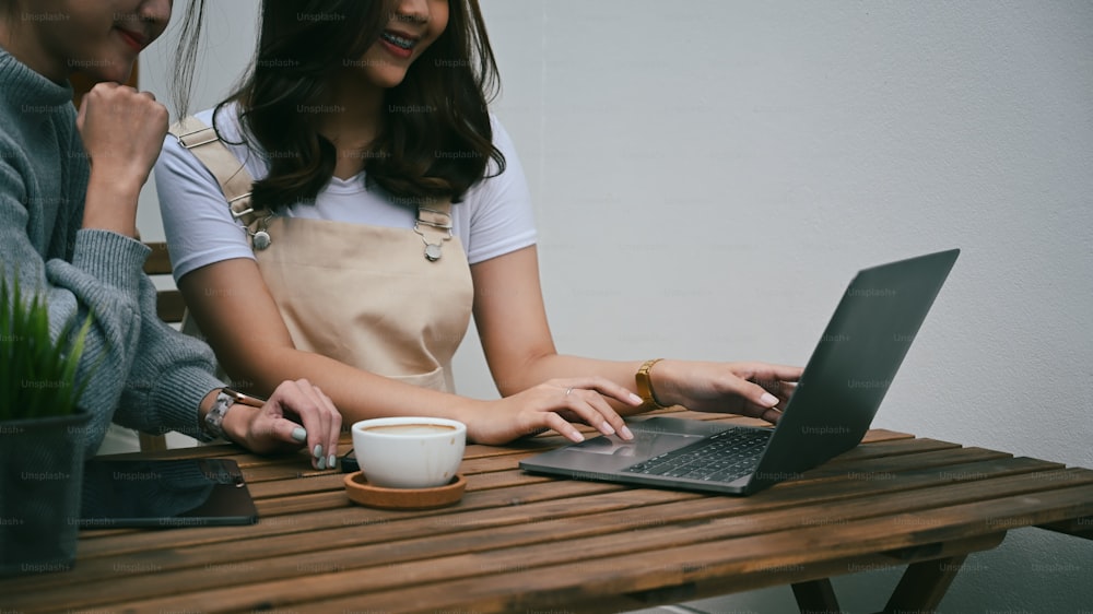 Dos jóvenes asiáticas que usan una computadora portátil mientras están sentadas en un café al aire libre.