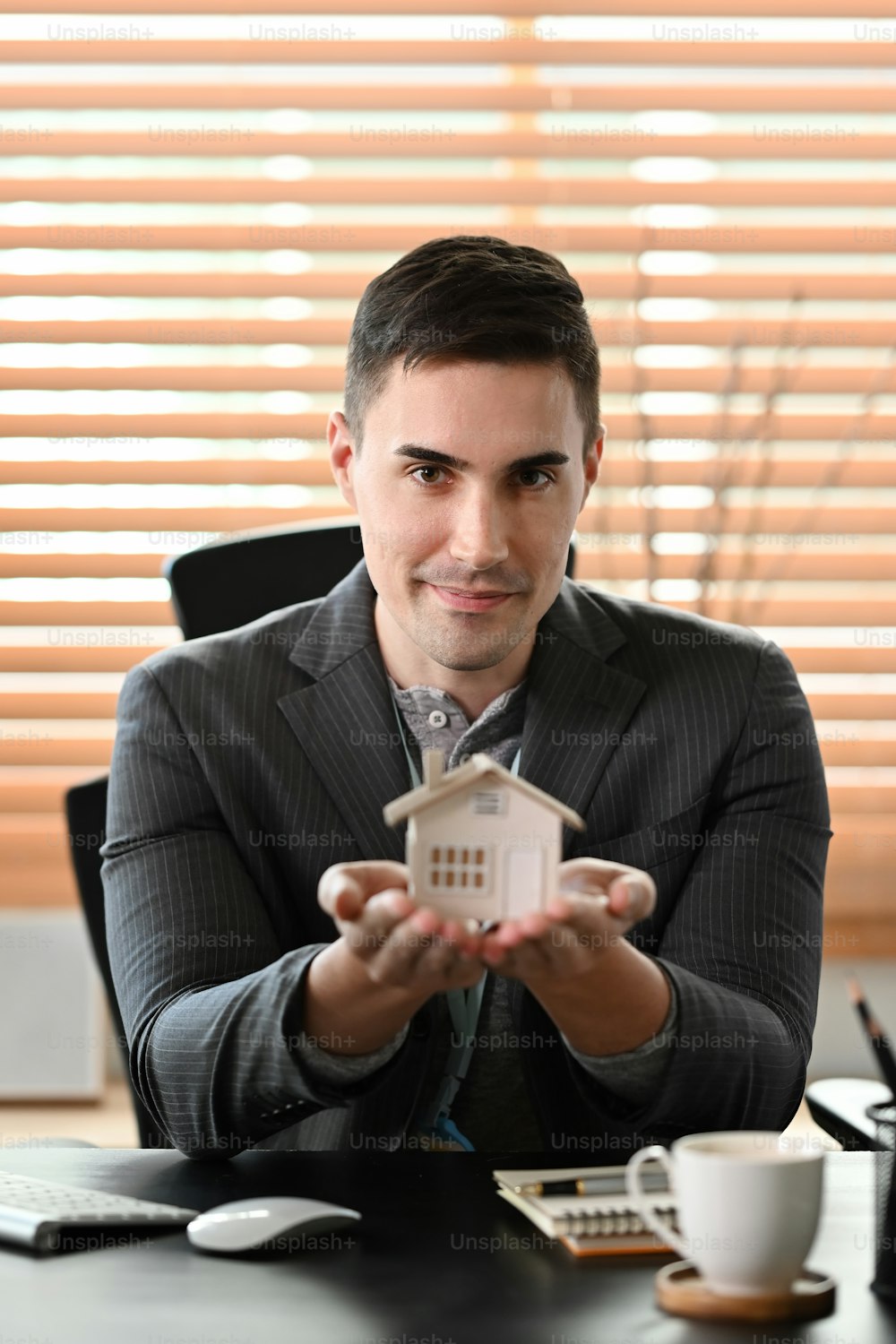 Portrait of real estate agent holding small house model and looking at camera. Real estate investment concept.