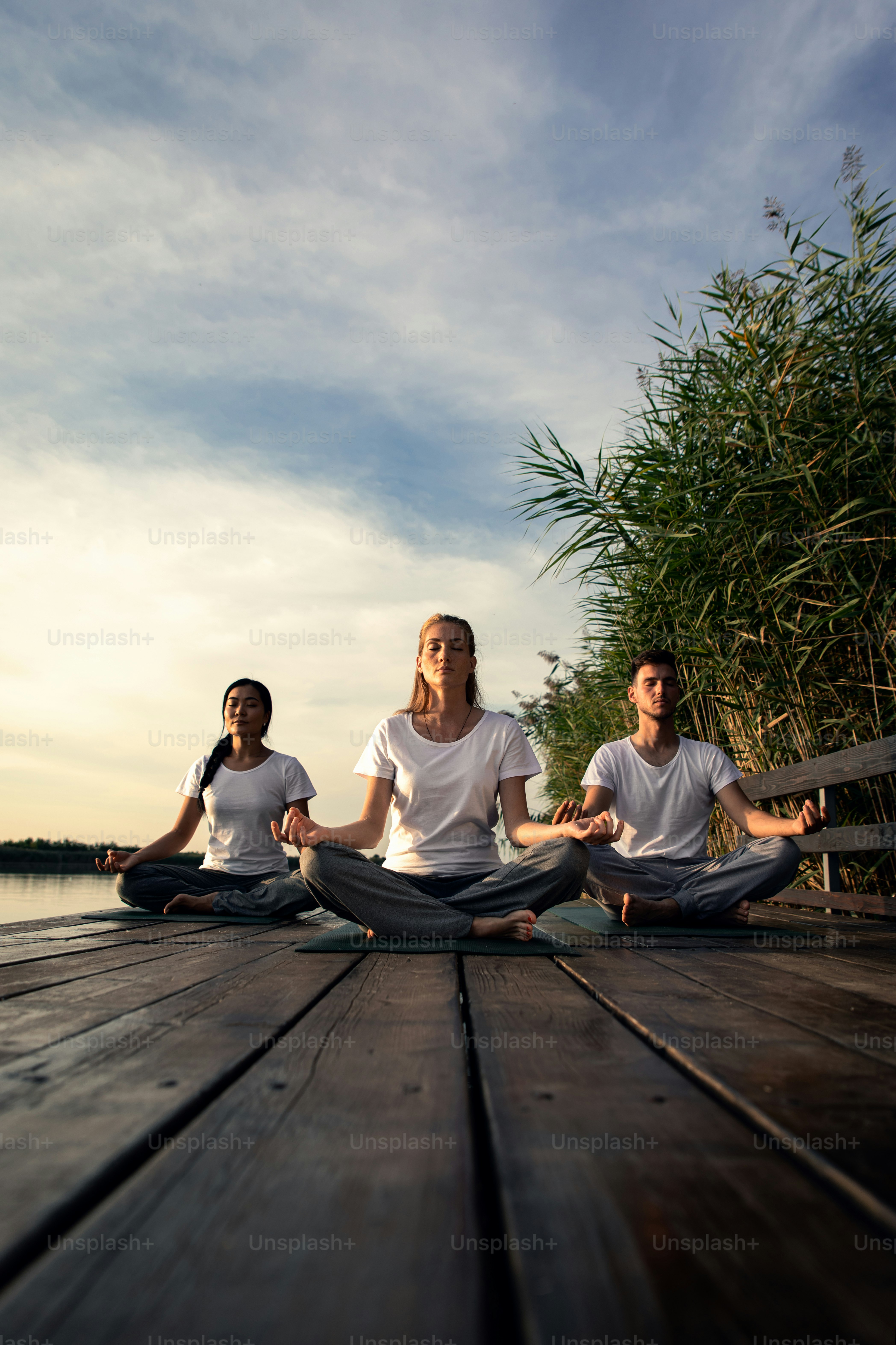 Group of people doing yoga exercises by the lake at sunset.