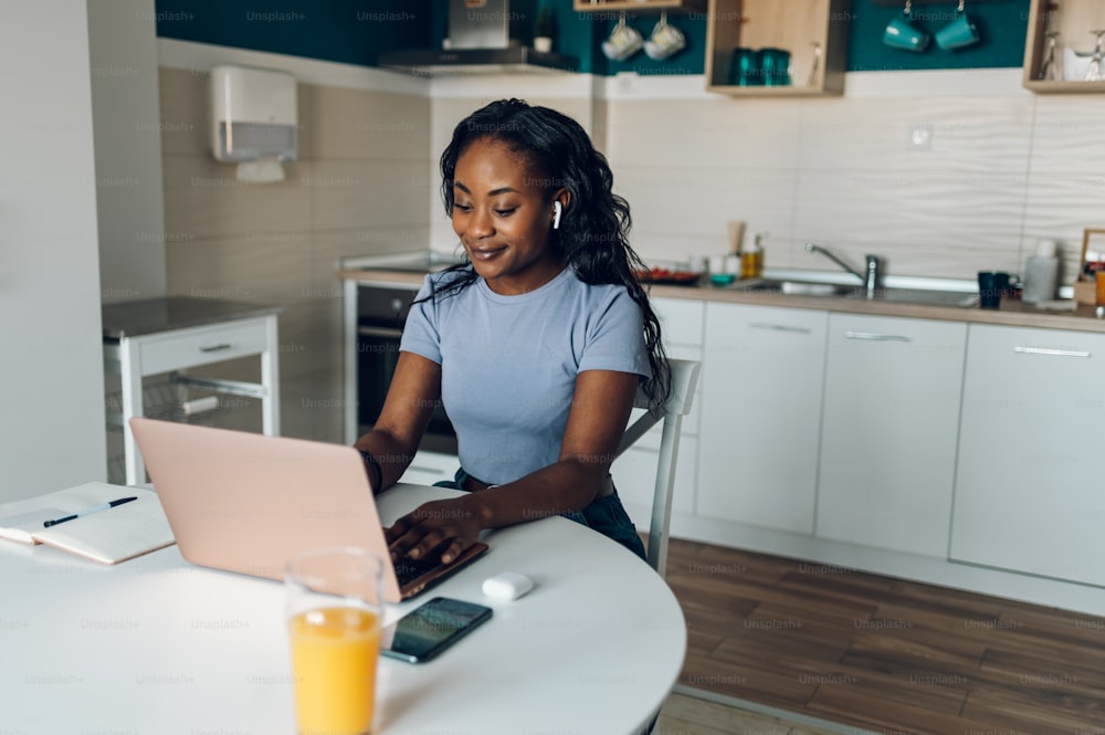若いアフリカ系アメリカ人の起業家の女性は、キッチンで自宅で仕事をしながら、新しいプロジェクトに取り組んでいます。スタートアップビジネスと新しいモバイル技術。