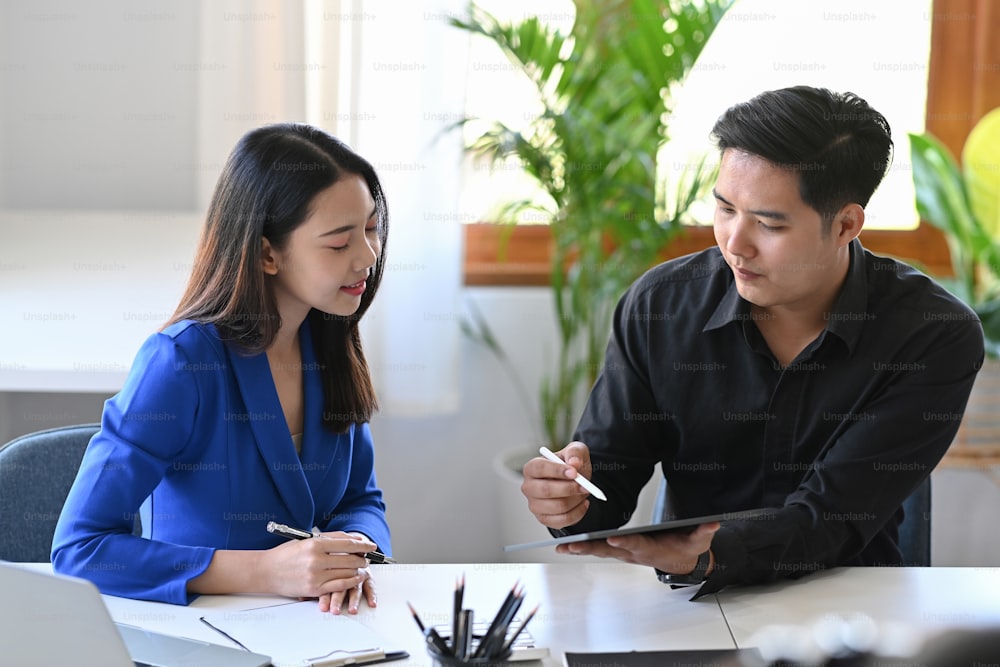 Businesspeople using digital tablet and discussing business strategy together at office.