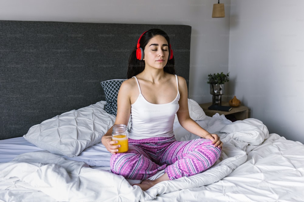 joven latina meditando usando auriculares en la cama en casa en México América Latina