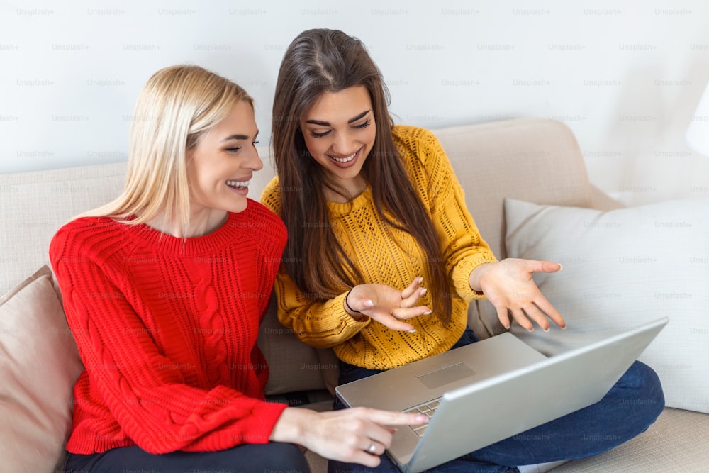 Portrait of a happy girlfriends surfing the net on laptop at home. Lovable blond and brunette girls having fun at home