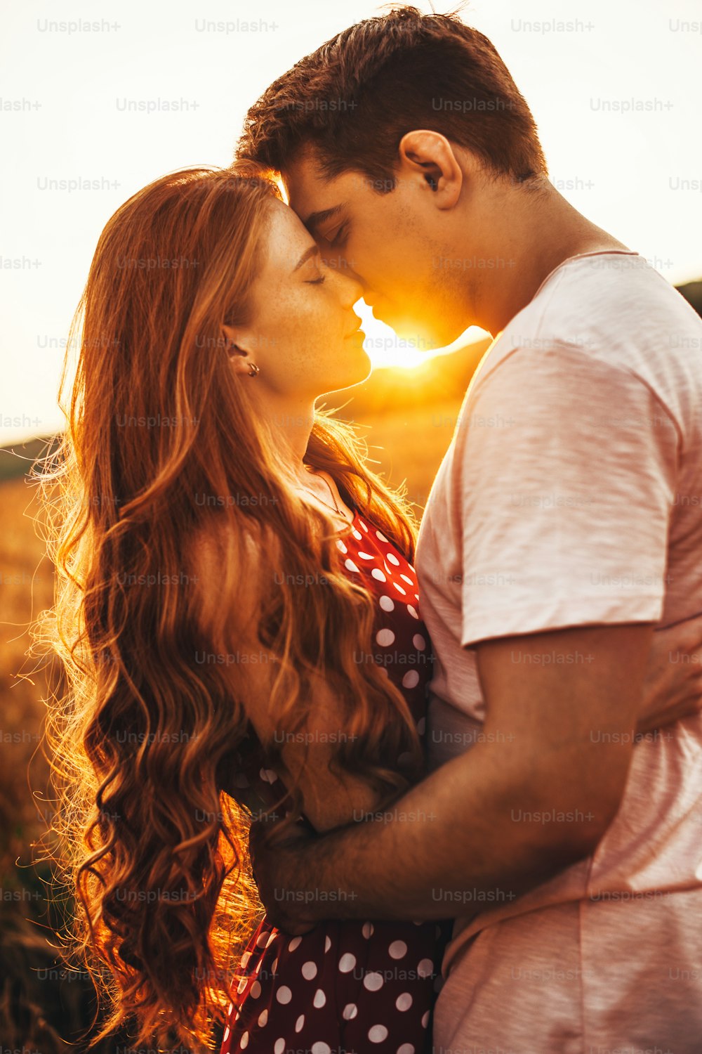 屋外の会議で夫にキスをする長い赤い髪の女性の横から見た写真。明るい背景を背景にポーズをとる
