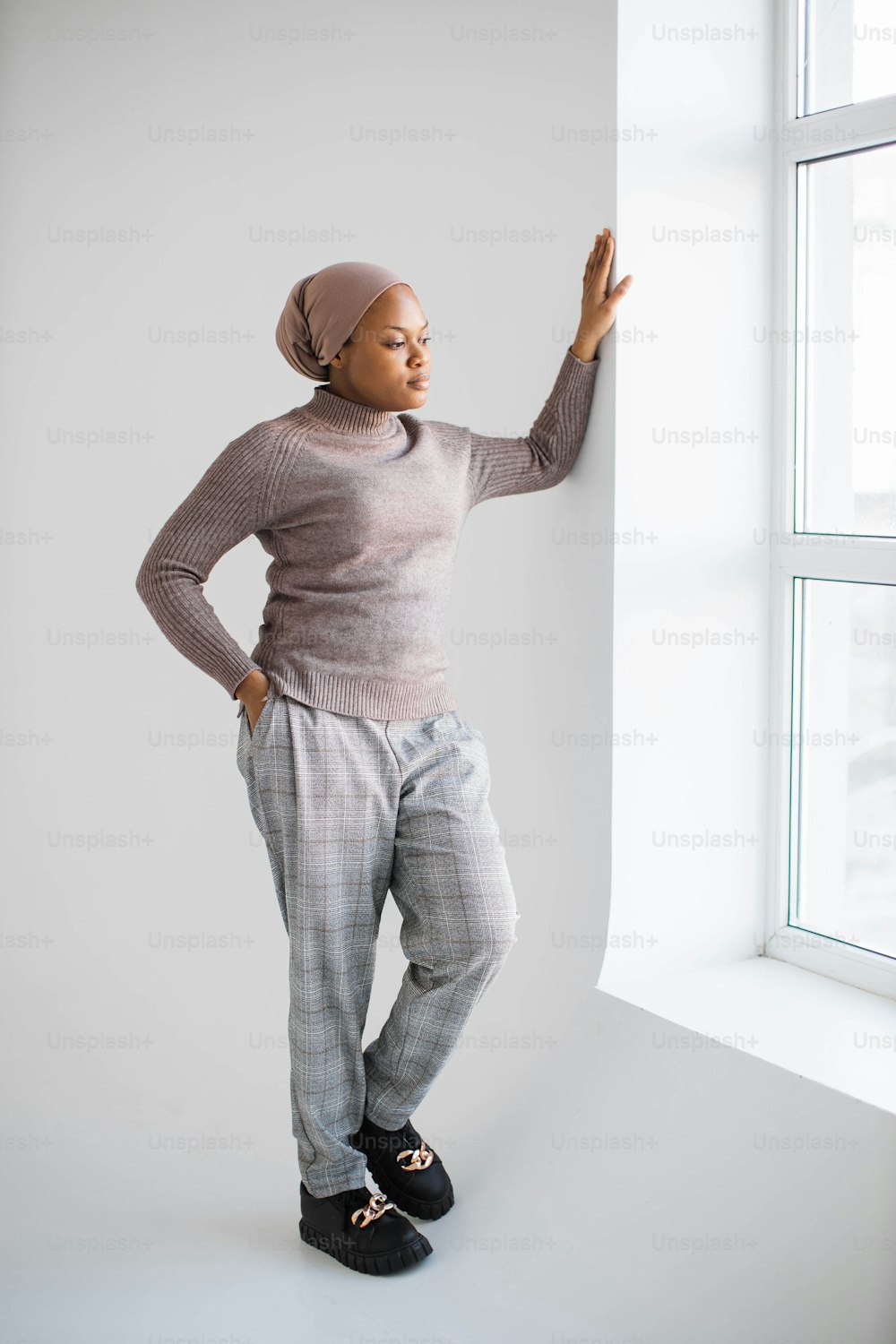 Attractive african american muslim woman in headscarf and casual clothes standing in studio with white background and looking at window. Concept of people and lifestyles.