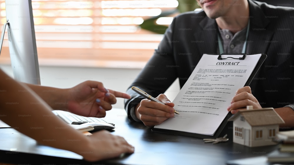 Foto recortada asesor financiero masculino que consulta con clientes sobre la nueva casa y muestra el documento del contrato.