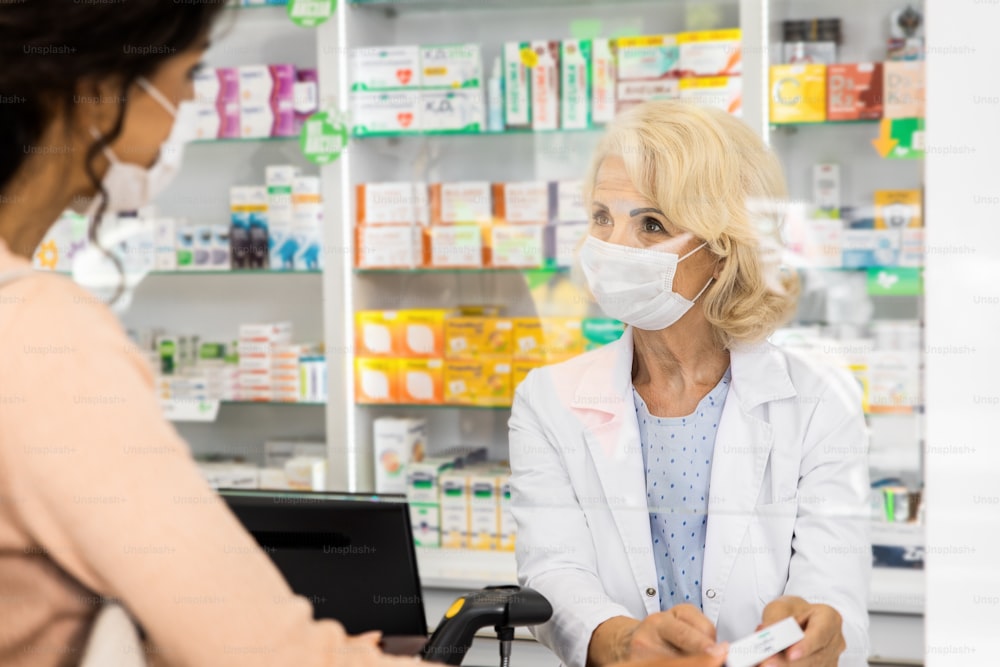 Farmacista senior che vende farmaci a una giovane cliente femminile nel negozio della farmacia.