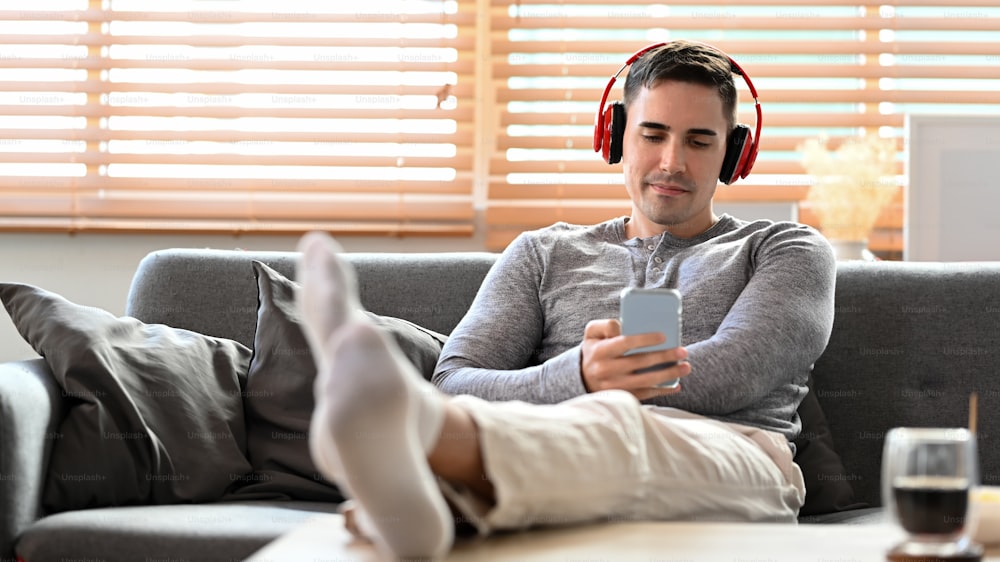Man wearing headphone and using smart phone on couch at home.