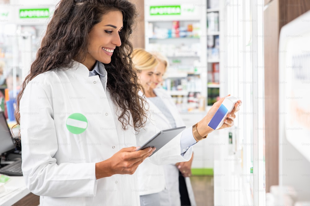 Junge Apothekerin, die in der Pharmazie arbeitet und ein digitales Tablet während der Inventur verwendet.