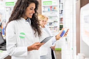 Young female pharmacist working in pharmacy using digital tablet during inventory.